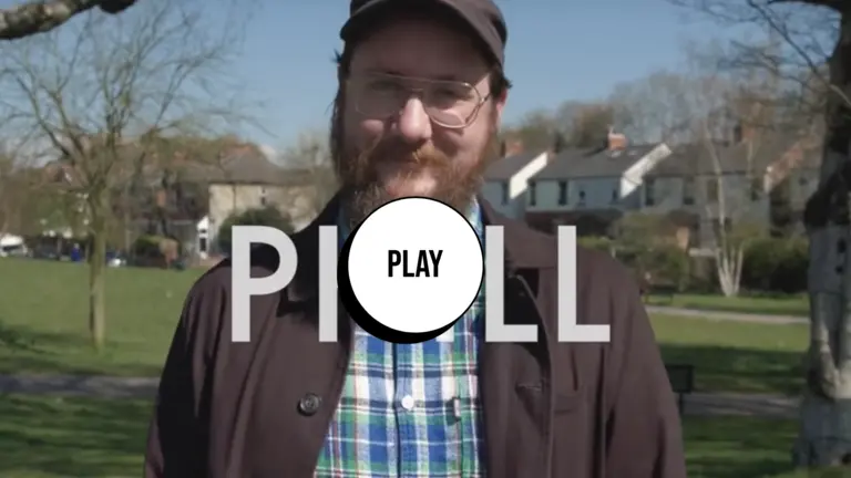 A person smiling at the camera with the words Phill before him. There's also a play button on top of it. 