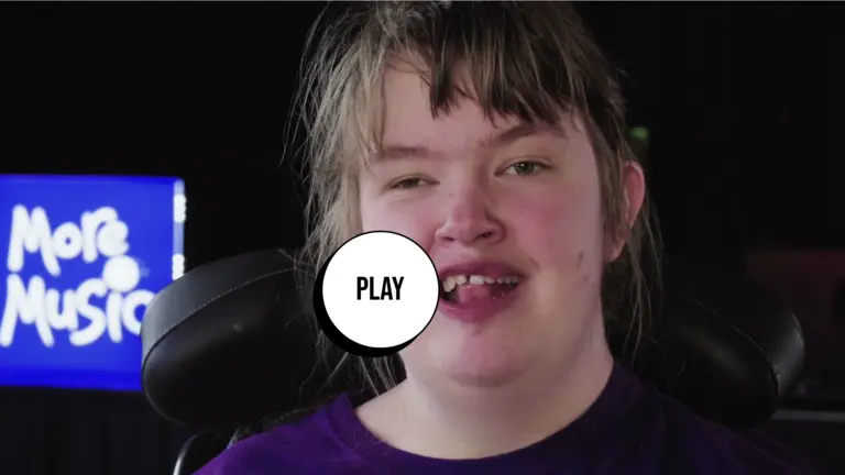 Person with a purple jumper talking to the camera. In the background, there's more music logo in white over blue. 