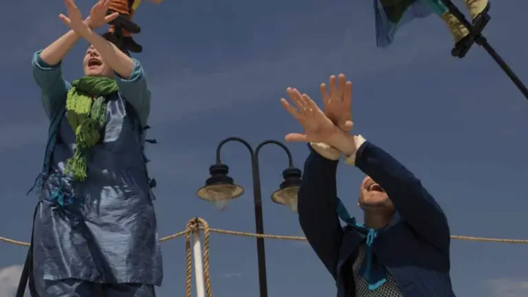 Two people in blue costumes participate in an outdoors event. They're both crossing and lifting their hands. 