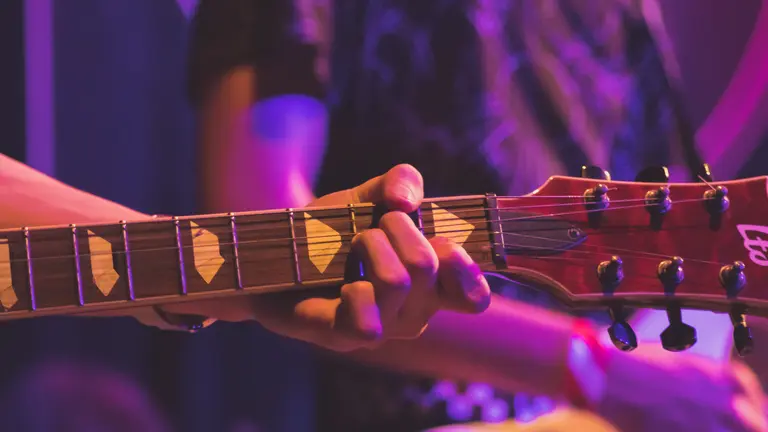 Close up of guitar neck with a hand playing it.