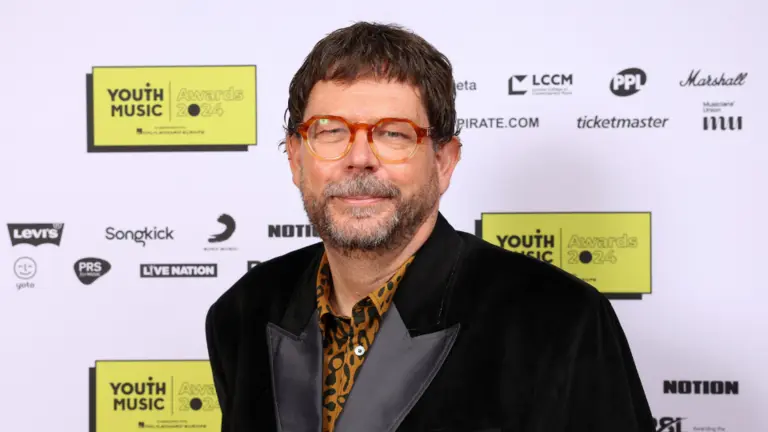 Matt Griffiths at the Youth Music Awards, wearing a black suit with grey lapels, a tiger print shirt, and red-rimmed glasses