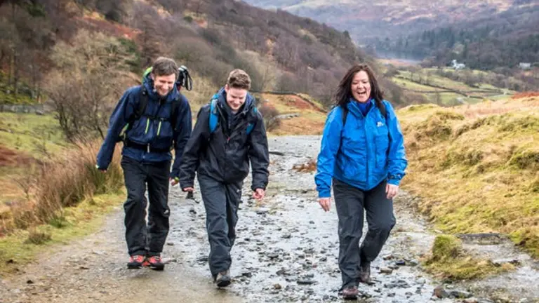three people trekking in a muddy trail in the mountains. they are all laughing and wearing trekking clothes