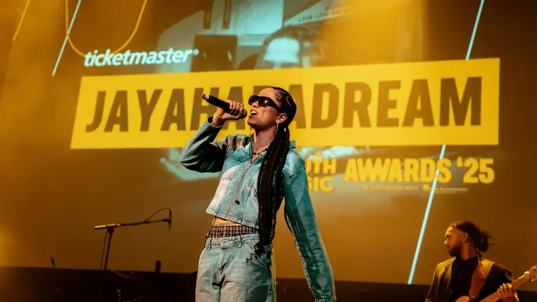 jayahadadream performing in a denim top and jeans. She's on stage at the YMAs 2025, performing with sunglasses on in front of a large screen with her name on it, singing into the mic