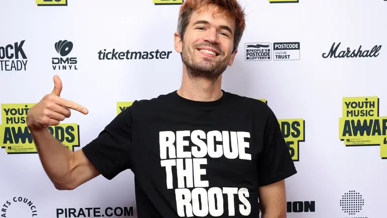 Ivo Graham at the YMAs2025 wearing a Rescue the Roots t-shirt and pointing to it smiling