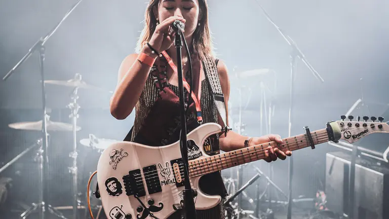 Young person on a stage, holding a mic and a guitar