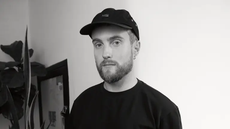 nicholas douglas wears a black t shirt and black supreme cap