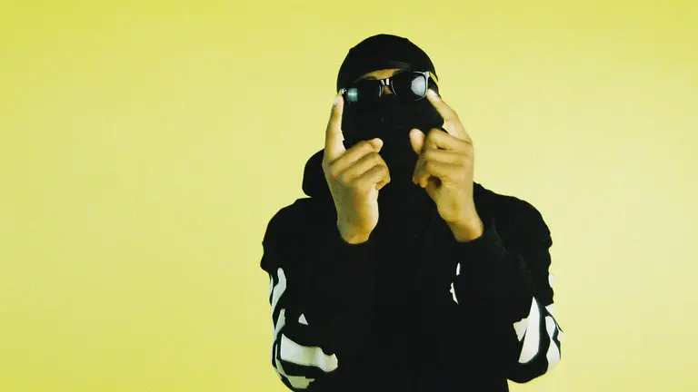 studiowyzz holds his hands up and poses for the camera. he wears a mask and sunglasses