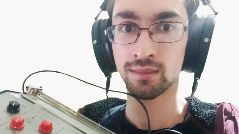 a man wearing glasses and headphones holds an electronic instrument