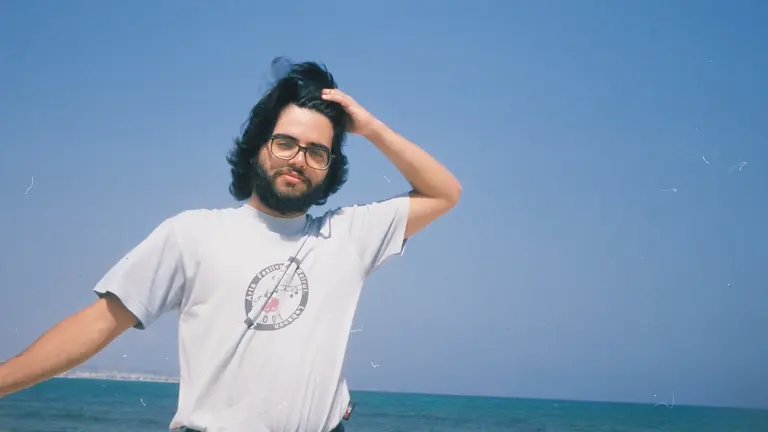 a man poses in a white t shirt against the sea