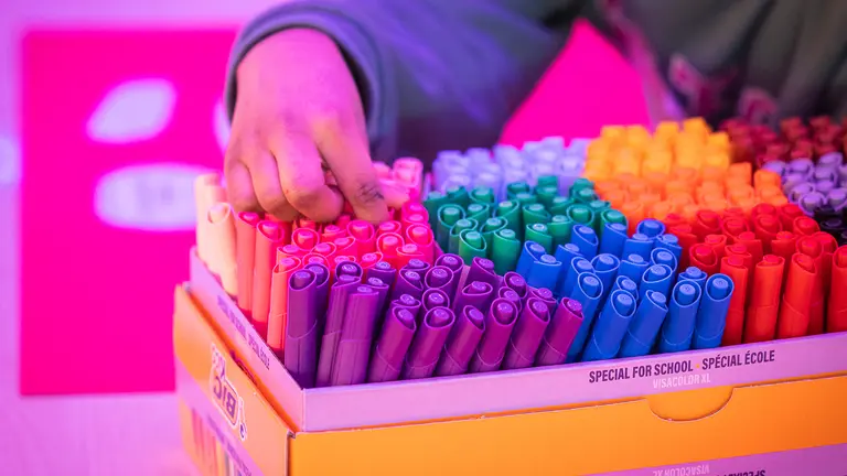 a box of different colour pens with a child's hand reaching to grab some
