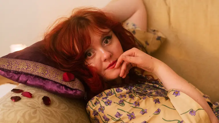 megan reclines on a sofa, resting her head on a pillow. she has red hair and a yellow top