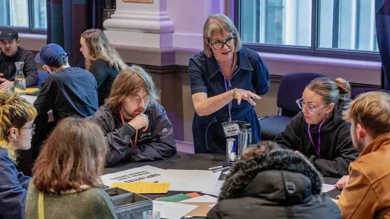 a group of people sit at a table and look thoughtful as one person stands and explains