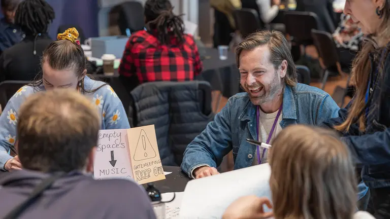 a man smiles broadly at a table of people 