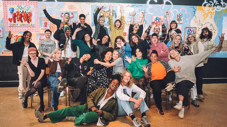 a group of people pose playfully in front of a collaged wall