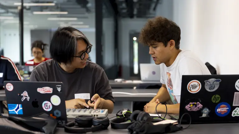 Two young people talking infront of two laptops