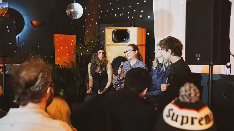 a panel of people sit on stage watched by an audience. a disco ball lights up the room