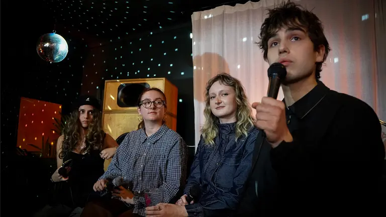 four people sit on sits in a room lit by a disco ball. the young man speaks into a microphone