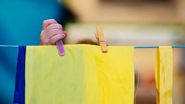 a child's hand pegging a yellow bit of material onto a line