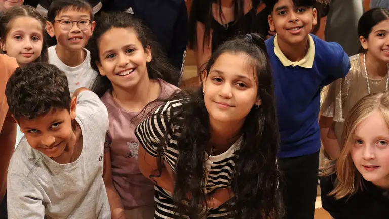 Lots of children in a music project all leaning forward and smiling at the camera