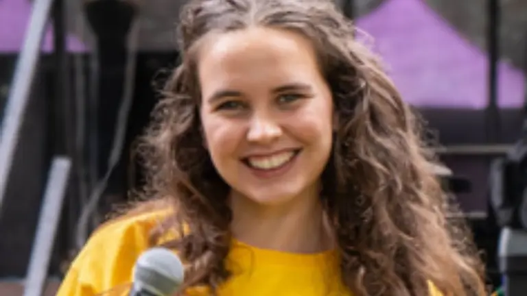 Grace with a yellow t-shirt on holding a microphone and smiling at the camera