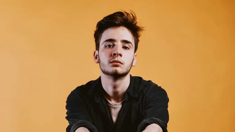Isaac looking straight down the camera with a neutral expression in front of a yellow backdrop