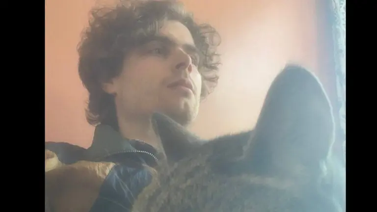man with a cat on his lap in front of an orange wall looking to the right of the camera
