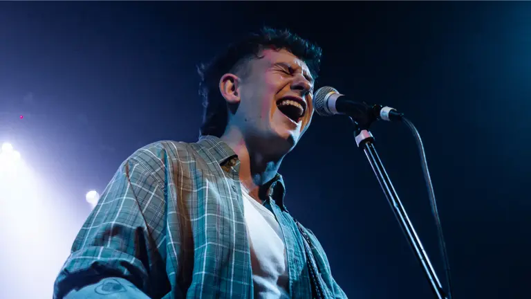 Brook on stage, singing into a microphone with closed eyes