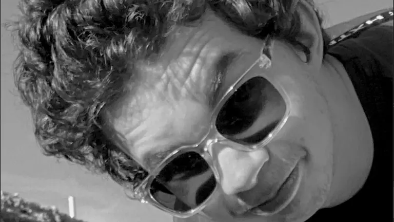 a man with sunglasses on with curly hair, in black and white