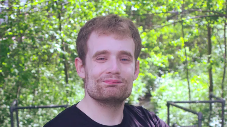 Patrick Wilde headshot, outside in front of trees and green leaves, smiling at the camera