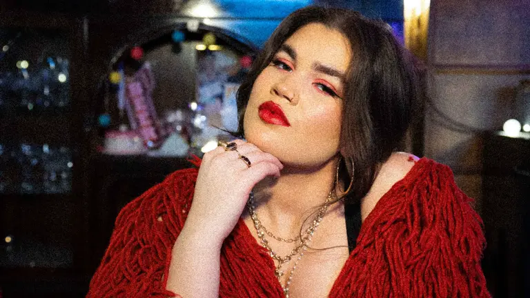 Rosie Larada wearing red, with red lipstick, resting her chin on her hand and staring into the camera