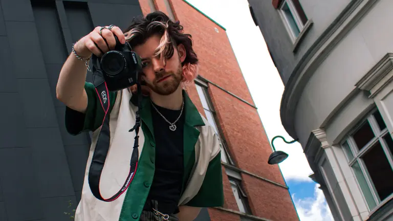 A person photographed from below, their holding a camera and pointing it