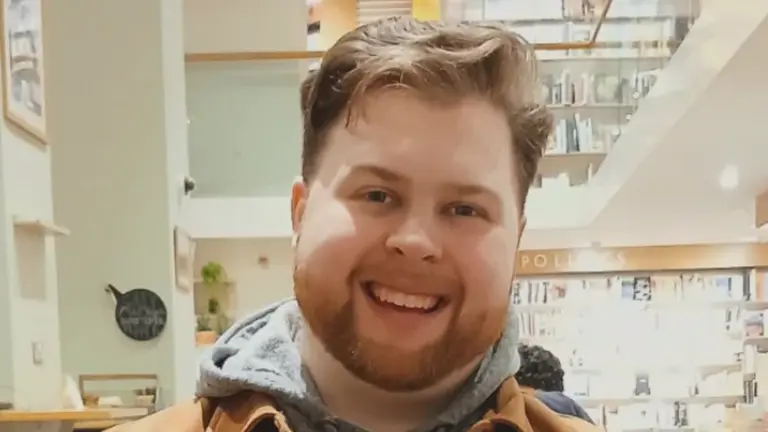 Tyler smiling at the camera in a jacket inside a library
