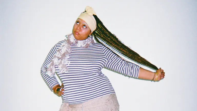 Vee Adu with a striped top on, holding her hair out to the side and looking above the camera