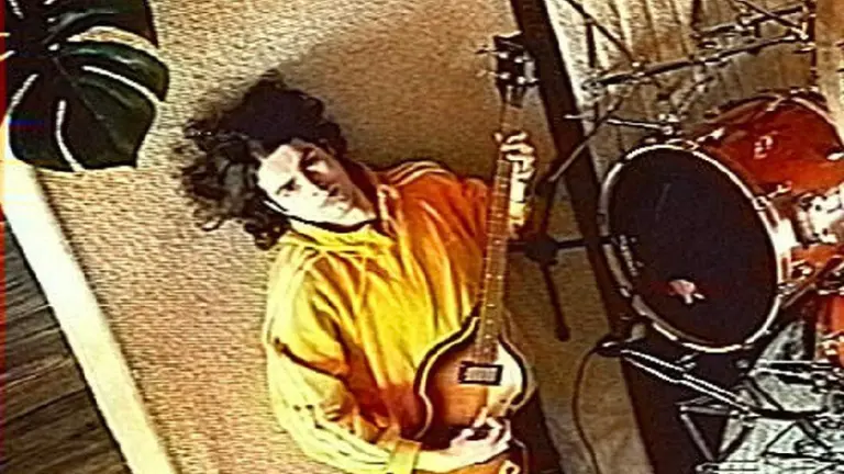 Jack Garrity lying down on a floor playing the guitar. Wearing a yellow top and lying next to a bass drum