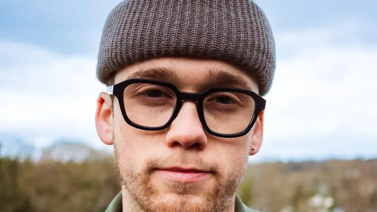 close up of a person with thick rimmed glasses, a grey beanie hat, taken outside 