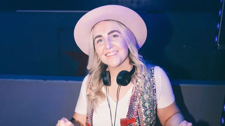 woman in a pink hat behind dj decks with headphones round her neck
