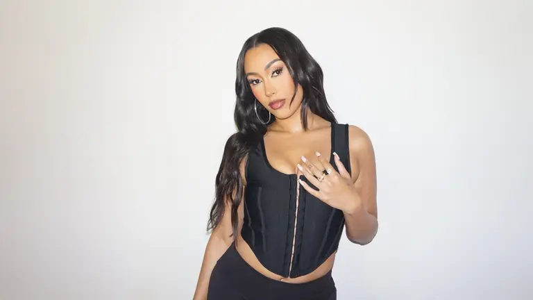 posing in front of a light wall with her left hand on her chest
