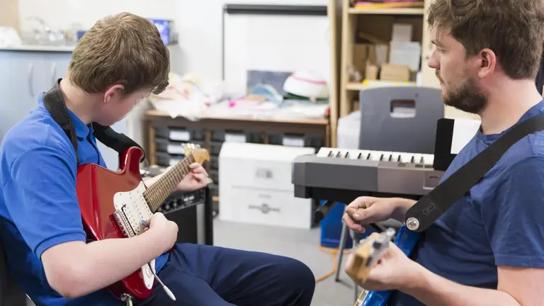 Two young people playing the guitar in a classroom environment