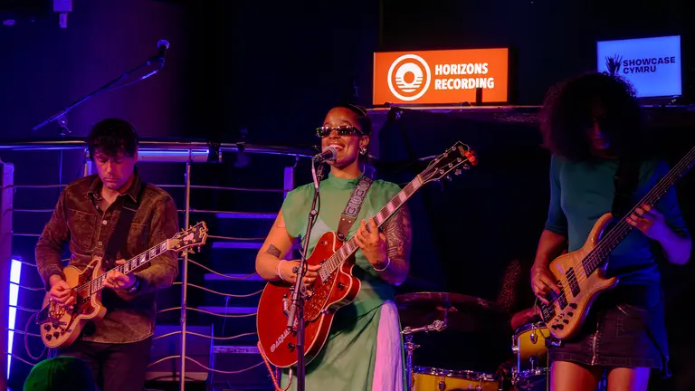 three musicians perform on stage. they all hold electric guitars.