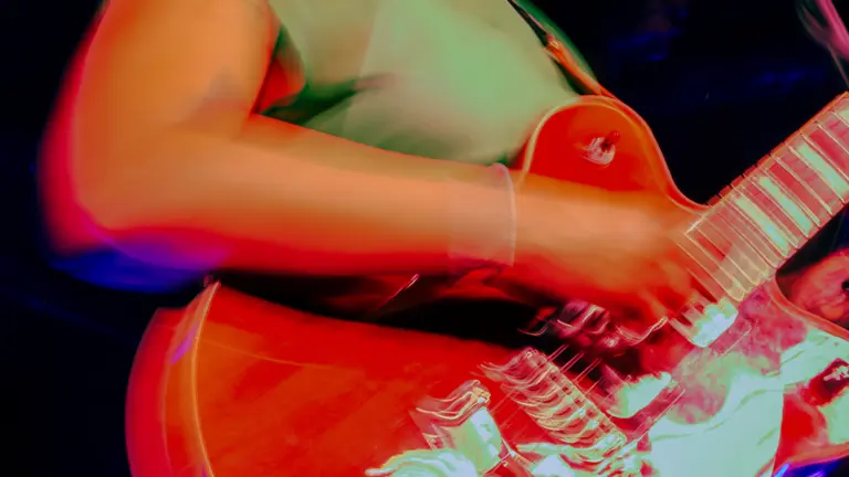 adjua wears a green dress, sunglasses, and holds a red electric guitar