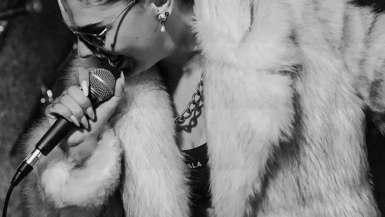 a black and white photo of boudicca wearing a fur coat and singing into a mic