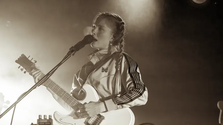 a sepia toned photo of maddie ashman singing into a mic and holding an electric guitar