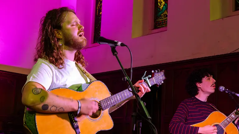 brodie barclay sings into a microphone while playing a spanish guitar