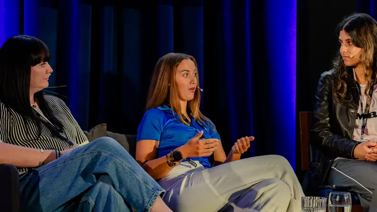three people sit in chairs as part of a panel. the woman in the middle is speaking while the other two look at her