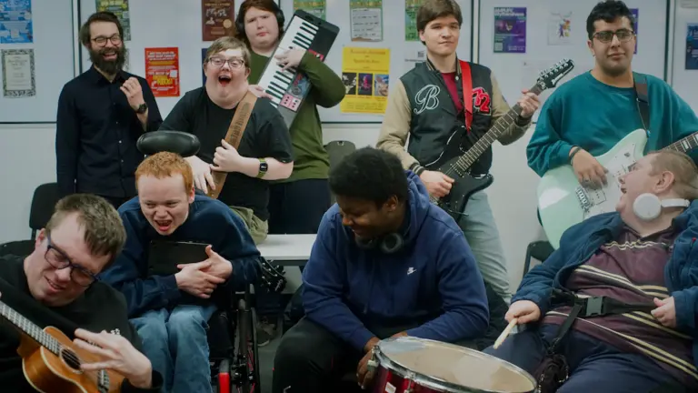 Nine people, several with visible Disabilities, play with music instruments in a classroom environment