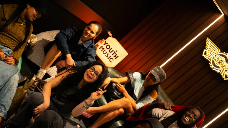 young people laughing and smiling in a recording studio in front of a Youth Music sign