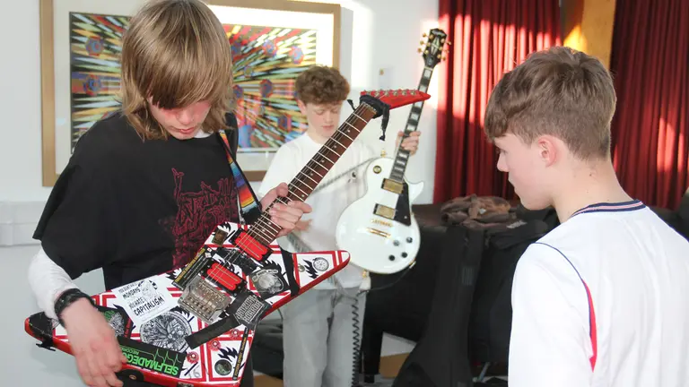 Three young people together playing guitar. 