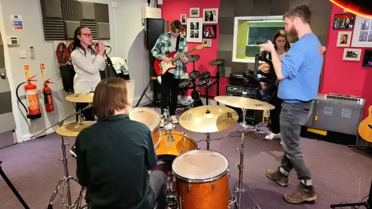 Five young people playing instruments together in a room.