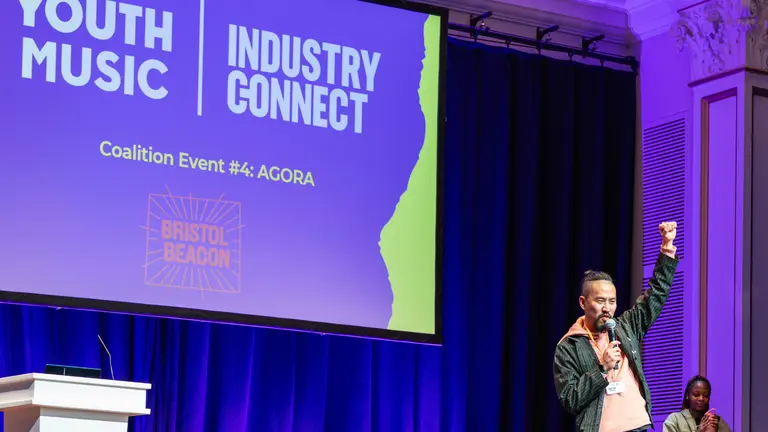 Dan Tsu on stage at an Industry Connect event, one hand in the air above his head, the other holding the mic