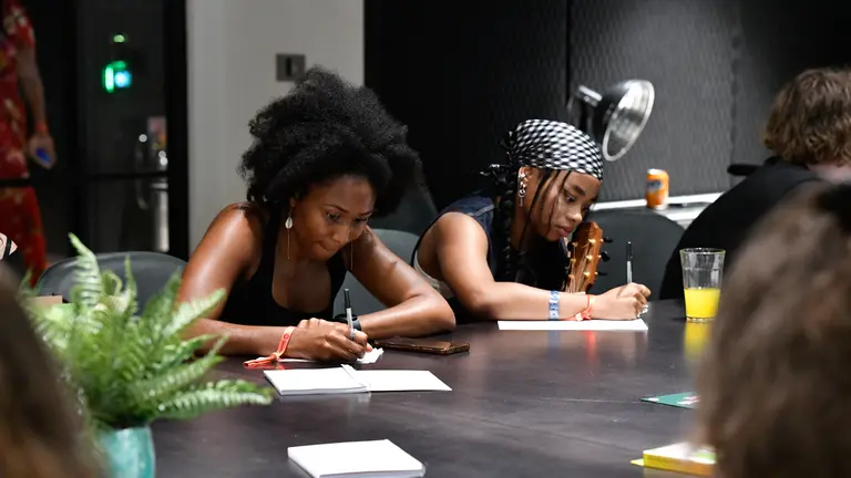 two women writing with pen and paper on a large desk